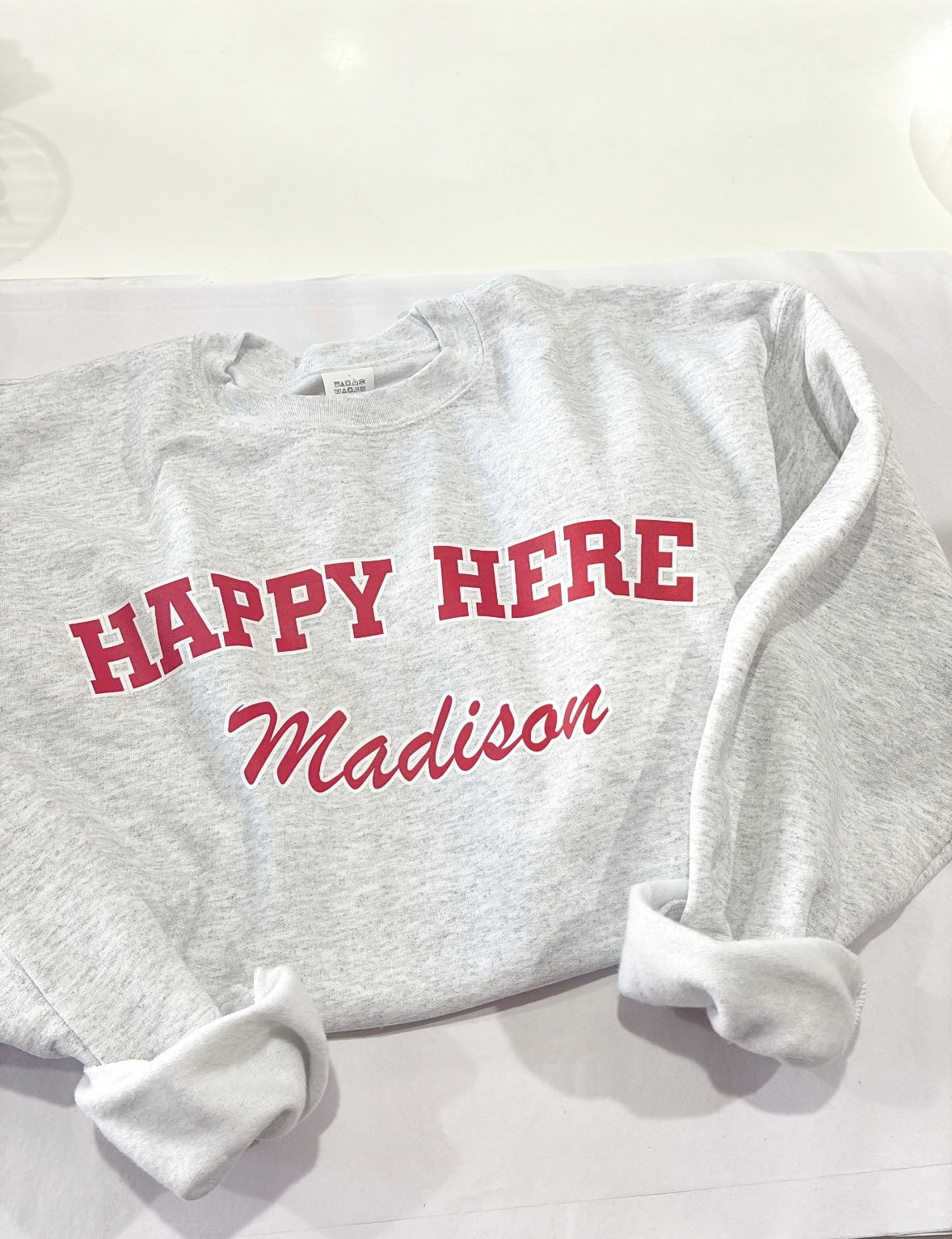 Gray sweatshirt with 'Happy Here Madison' text on a white background