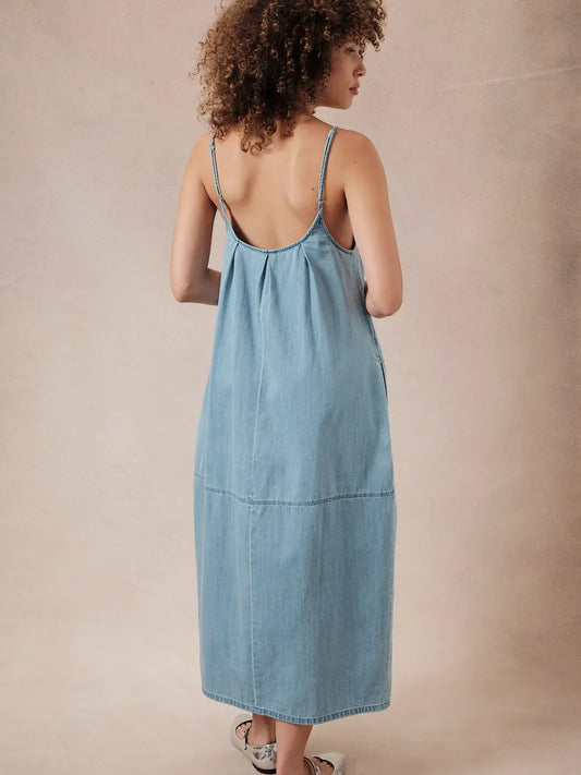 back view of a woman wearing a light blue barrel denim dress against a beige background