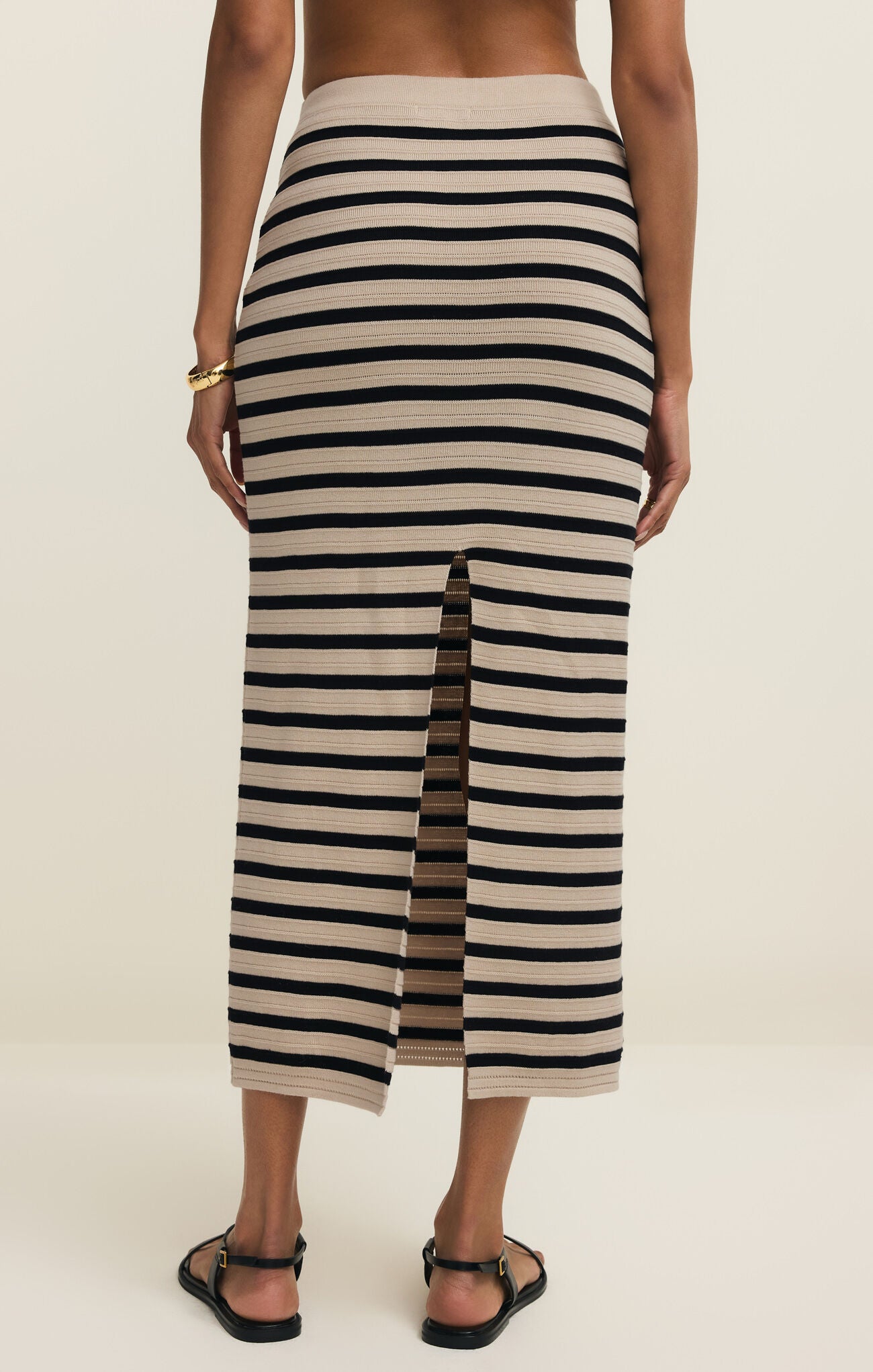 Back view of woman wearing a black and white striped skirt on a plain background