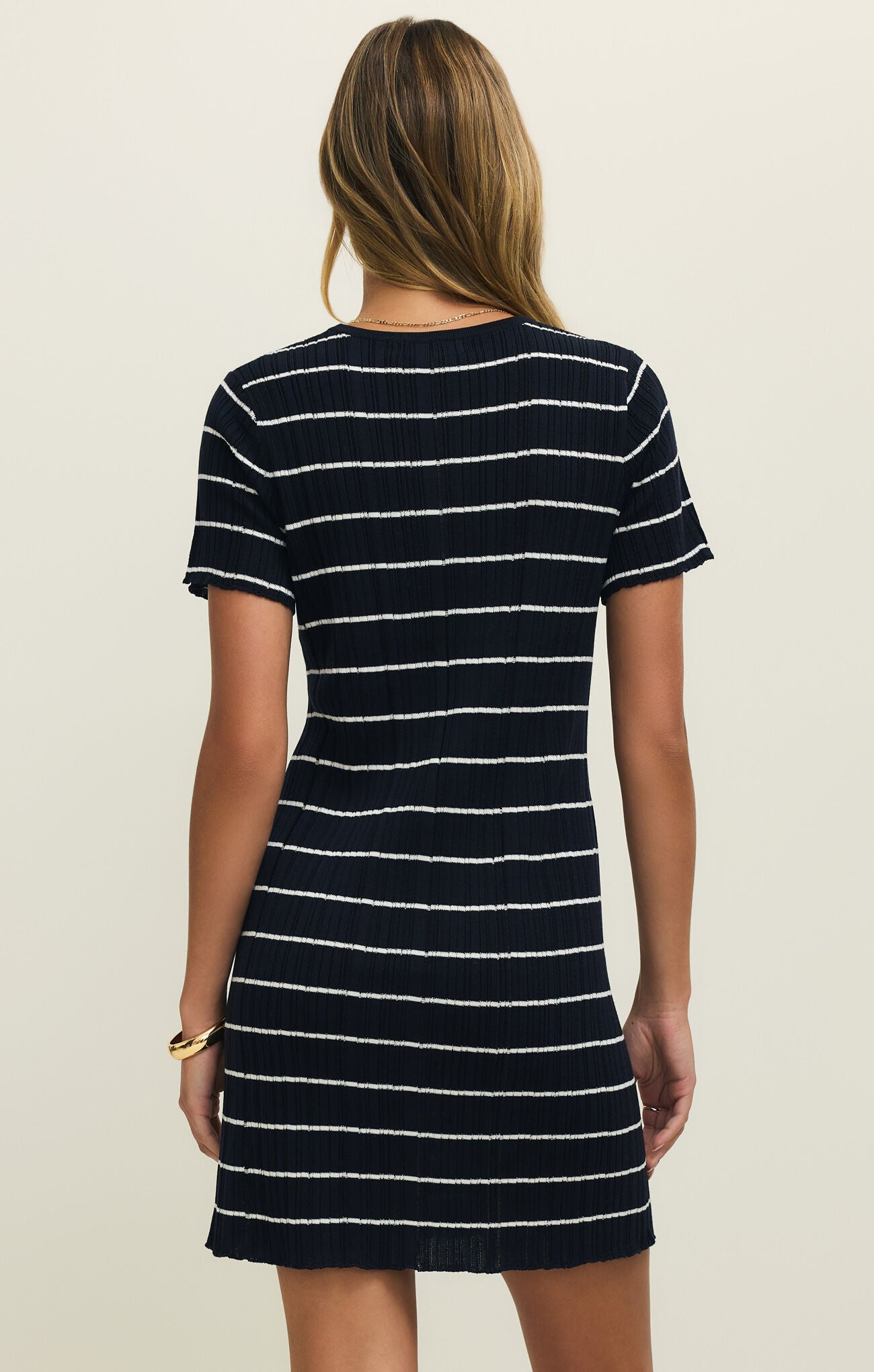 Back view of a woman wearing a navy and white striped mini dress against a plain background