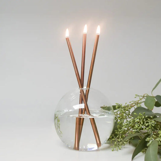 Candle holder with three lit candles in a clear vase on a white background