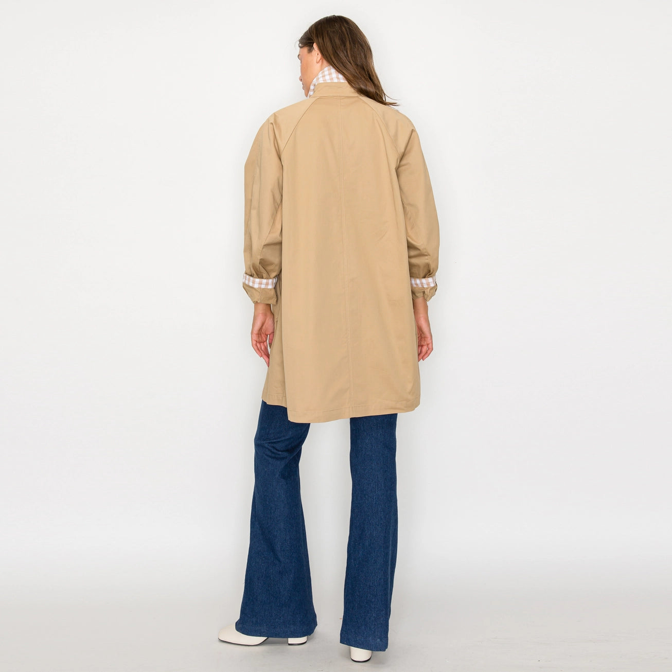 Back view of a woman wearing a beige mid-length trench coat on a white background