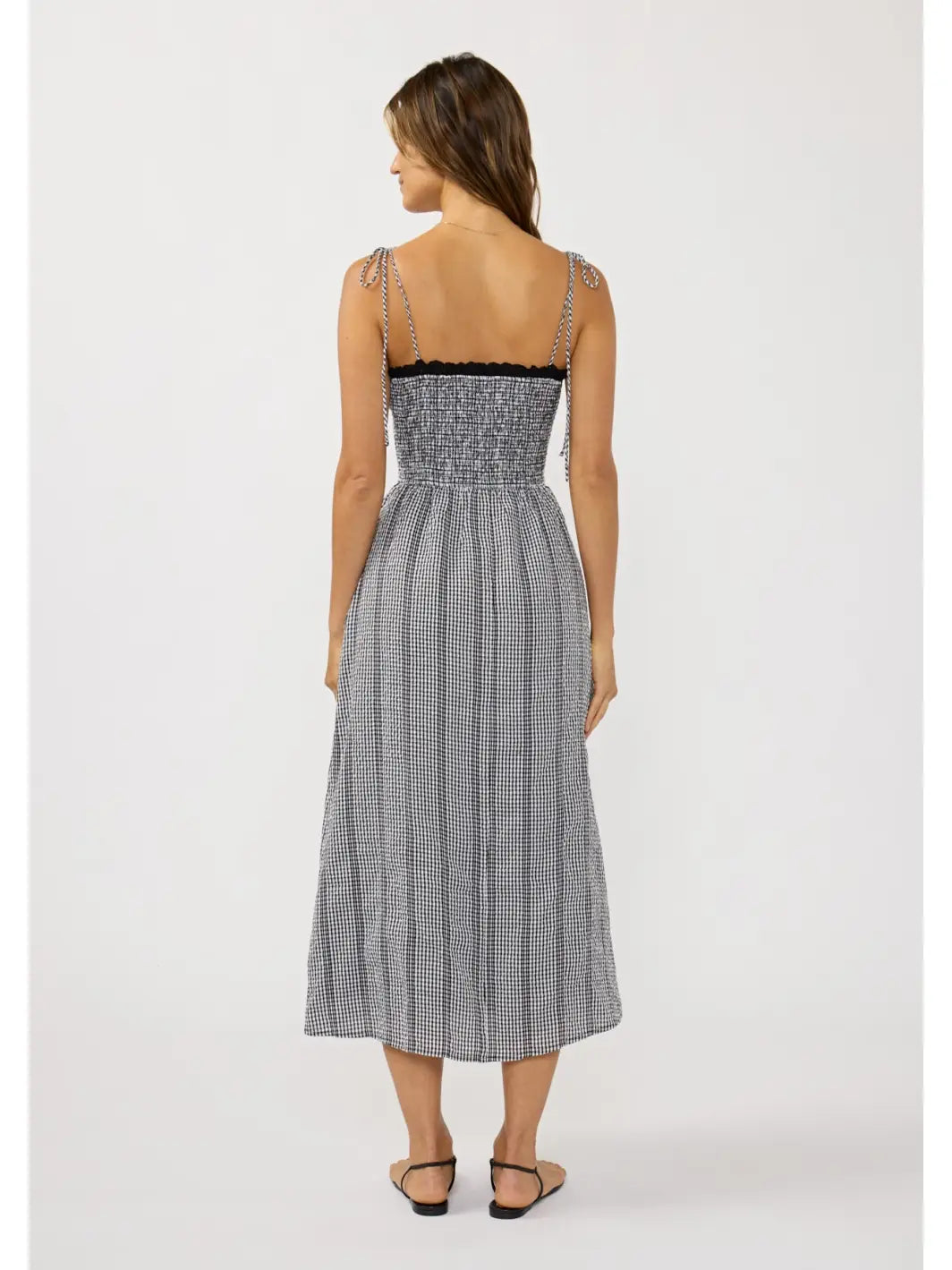 Back view of a woman wearing a black and white gingham checkered midi dress with spaghetti straps.
