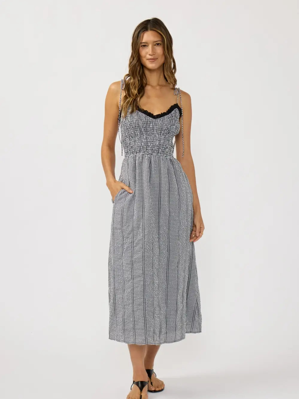 Woman wearing a black and white checkered gingham dress with spaghetti straps, flowy bottom.