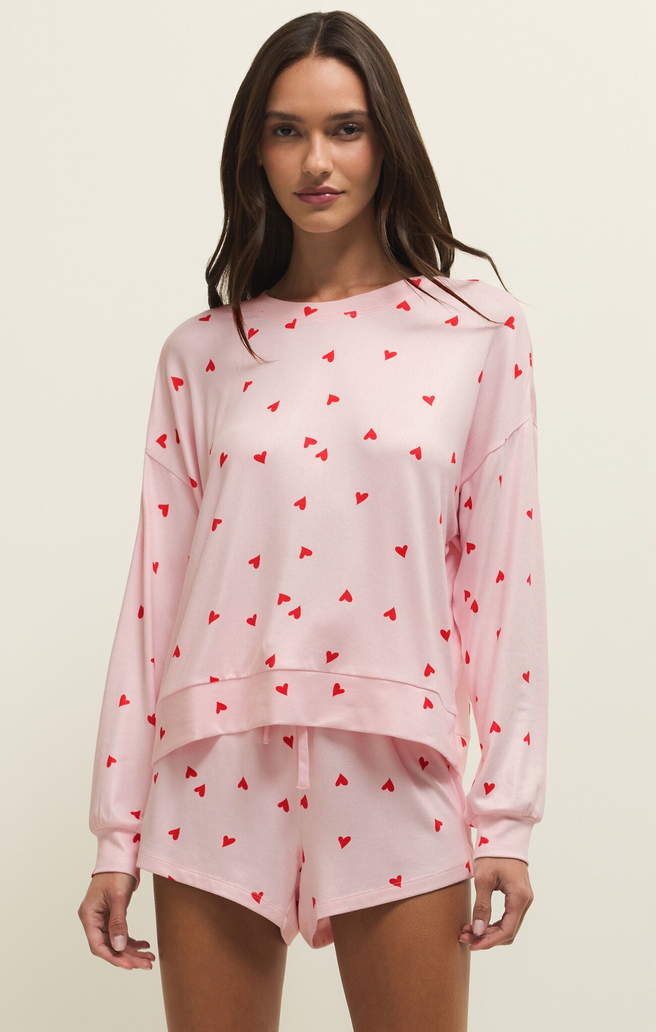 Woman wearing a pink pajama set with red heart patterns on a beige background