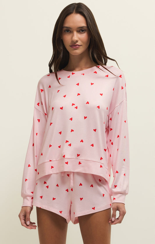 Woman wearing a pink pajama set with red heart patterns on a beige background