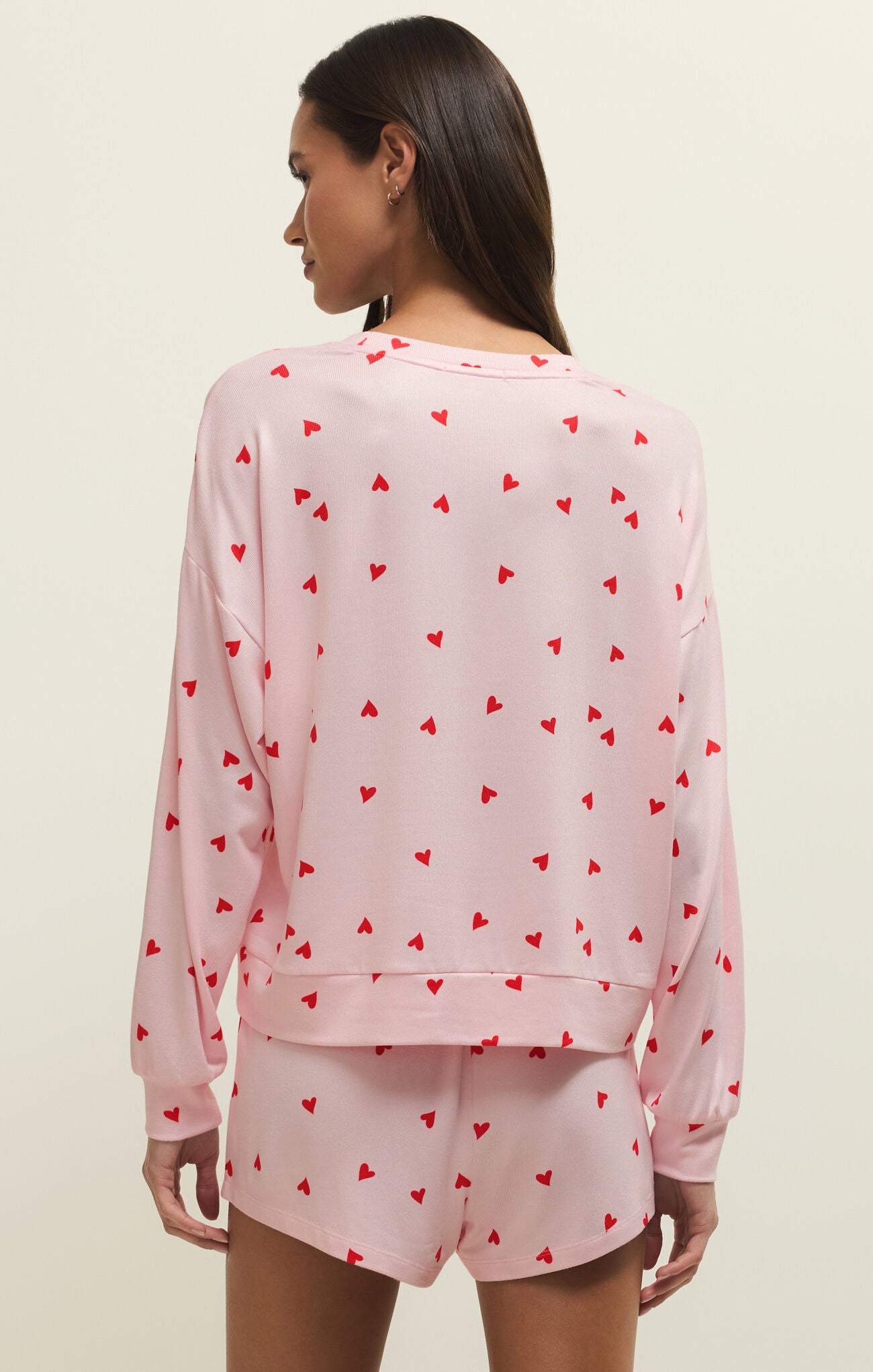 Back of  a woman wearing a pink pajama set with red heart patterns on a beige background