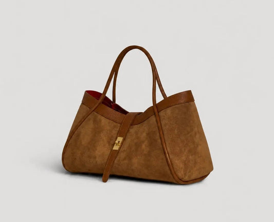 A brown suede tote bag with brown leather handles and trim, featuring a small gold-tone lock on a strap, set against a light gray background.
