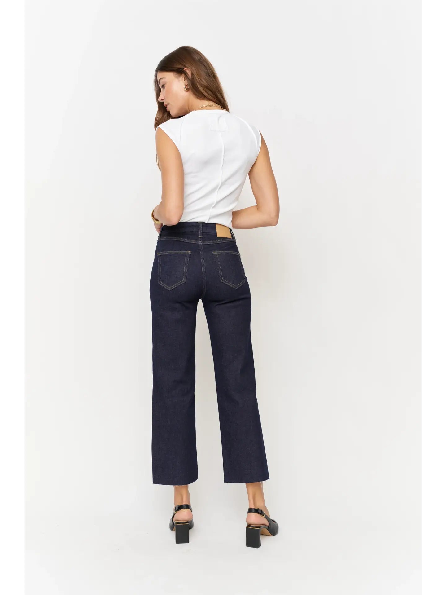 Back view of woman wearing high-rise denim wide leg crop, fitted through the hip, zipper fly, and a cropped raw hem.