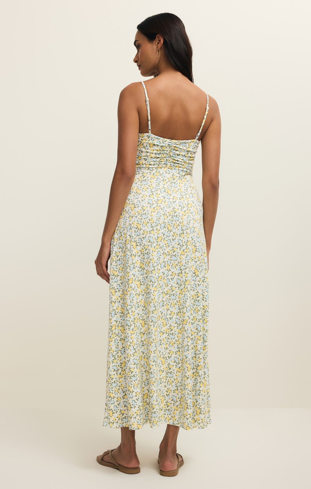Back view of a woman wearing a floral maxi dress with spaghetti straps on a plain background