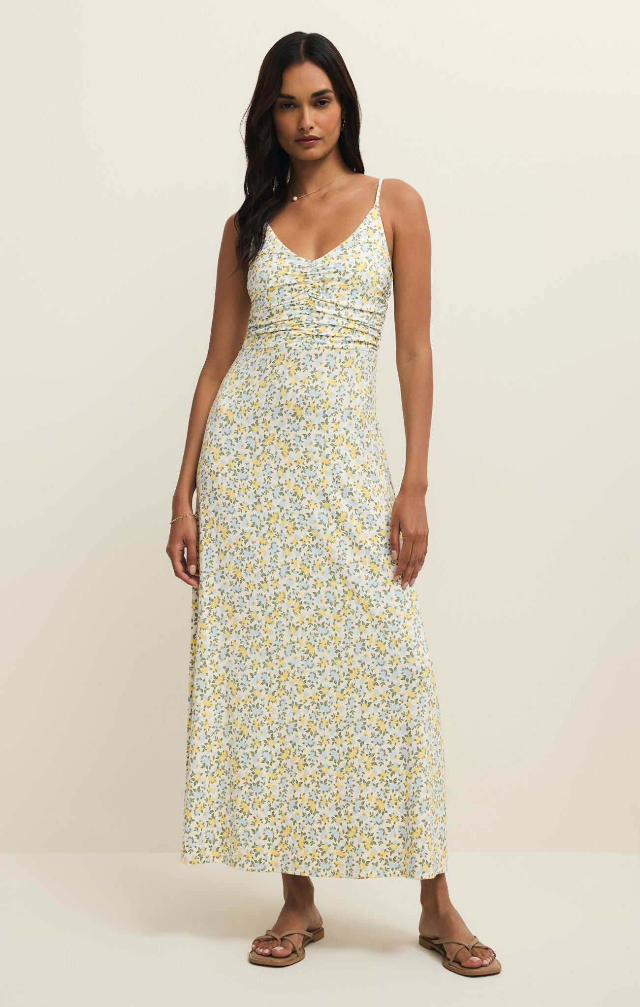 Woman wearing a floral maxi dress with spaghetti straps on a plain background