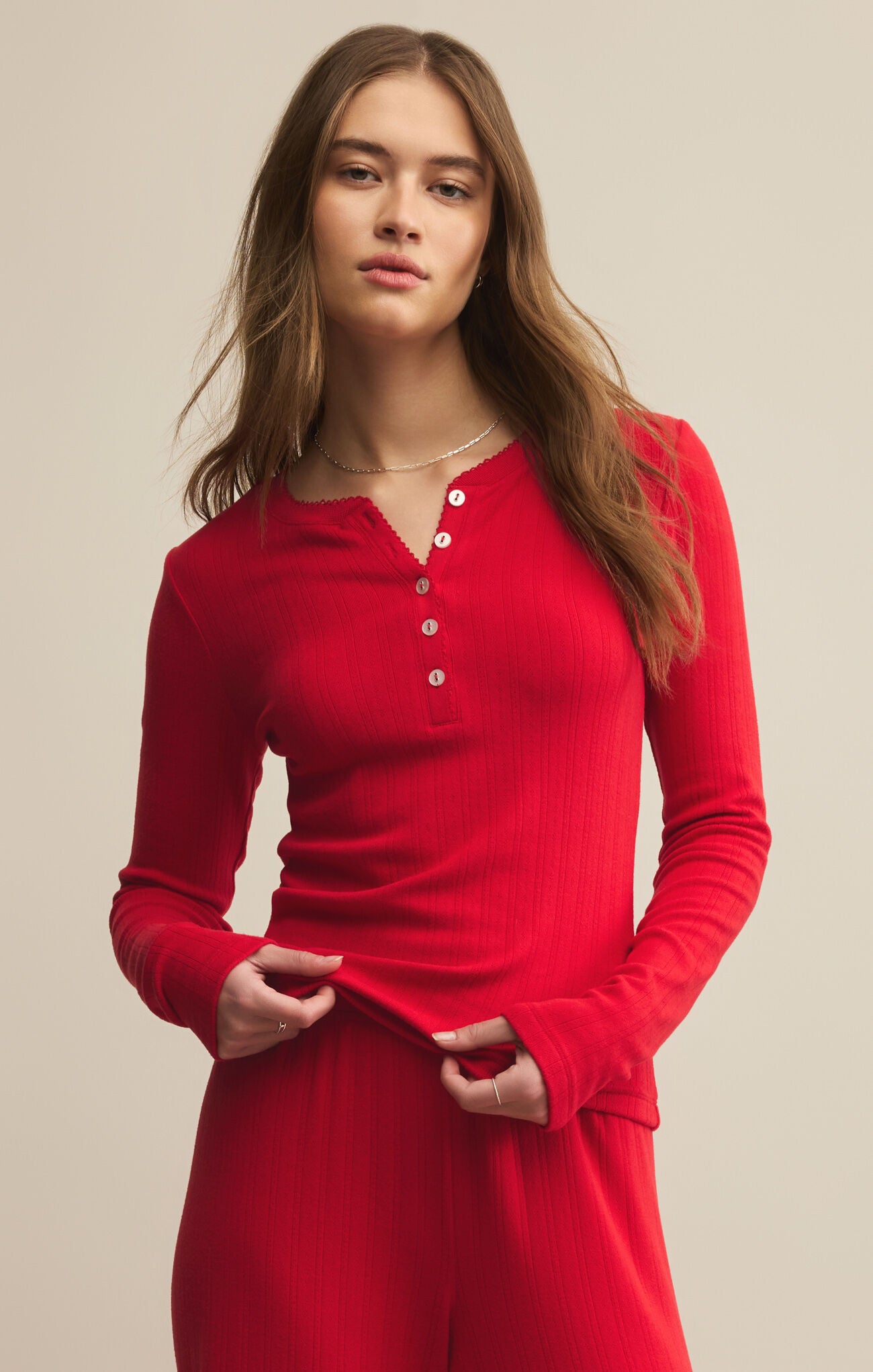 Woman wearing a henley red long-sleeve top with buttons on a beige background