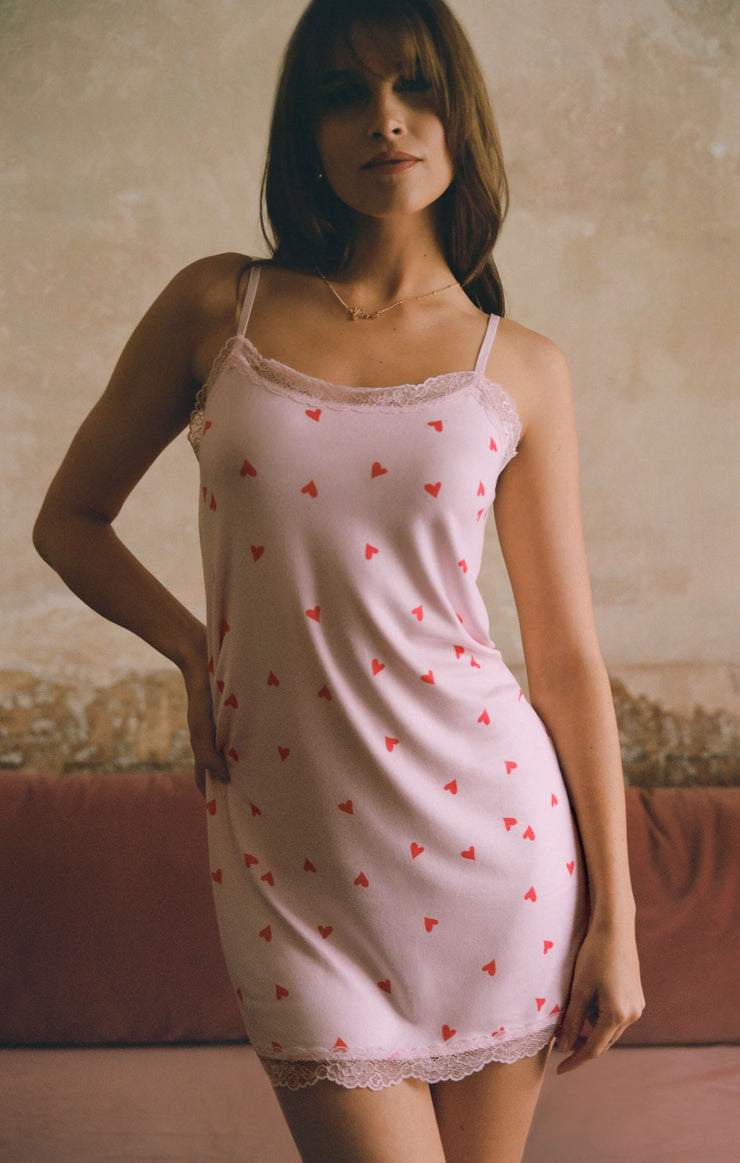 Woman wearing a pink silky jersey chemise with heart patterns in a room.